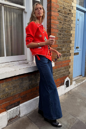 Cardigan Mystical rosso ricamato abbinato a jeans blu a gamba larga e stivali neri all'aperto.