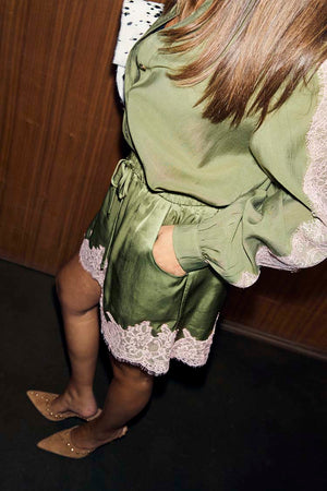 Shorts in pizzo verde oliva e rosa abbinati a una camicia coordinata e scarpe beige a punta.