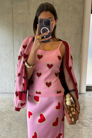 Top a canotta in maglia rosa con cuori rossi, abbinato a cardigan e gonna coordinati in un selfie.