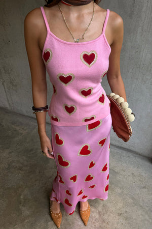 Canotta rosa in maglia con cuori rossi, abbinata a gonna midi coordinata e scarpe color cuoio.