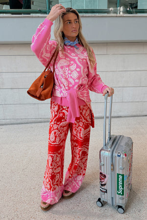 Pink Bandana Copenhagen Jumper and matching red joggers co-ord, styled with a necktie and silver suitcase.
