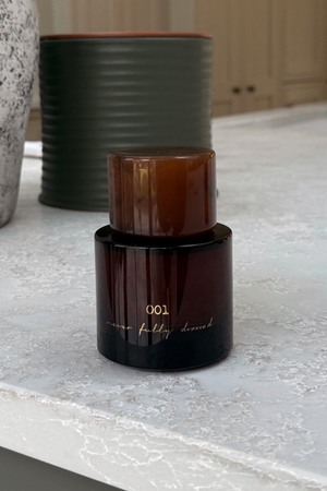 NFD Eau De Parfum 001 in a dark amber glass bottle with a tortoiseshell cap on a white marble surface.
