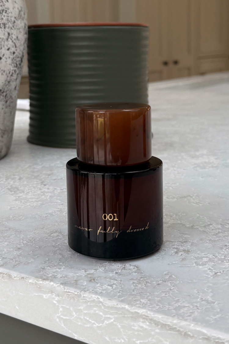 NFD Eau De Parfum 001 in a dark amber glass bottle with a tortoiseshell cap on a white marble surface.
