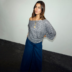 Gunmetal Sequin Tilly Top styled off-the-shoulder with dark denim wide-leg jeans on a model.