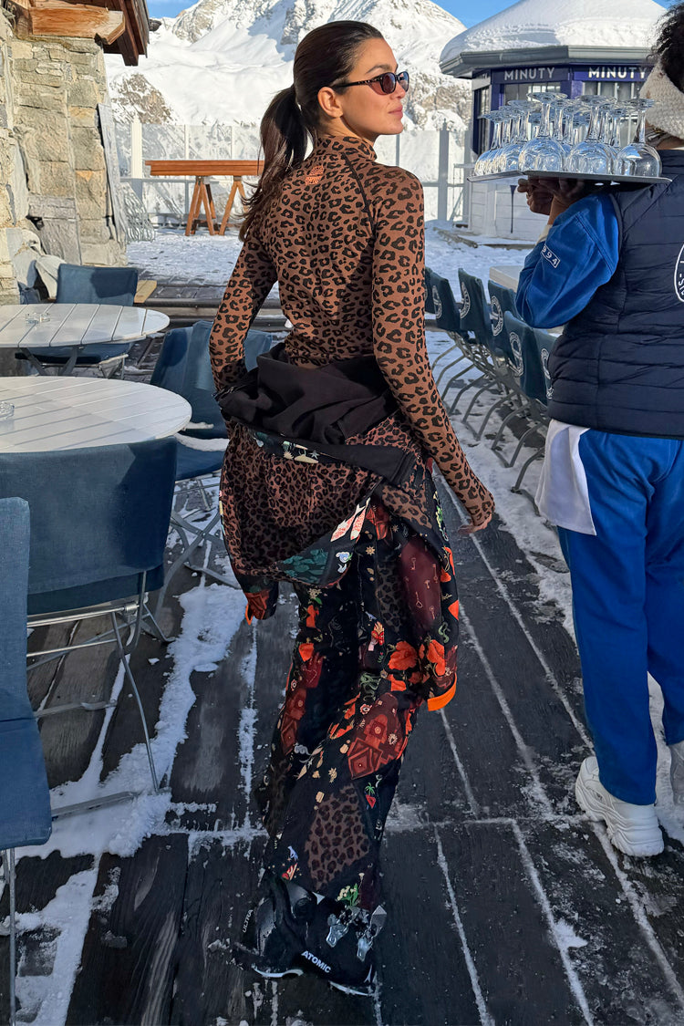 Night Garden Ski Suit with leopard and poppy motifs, worn by a model on a snowy mountain terrace.