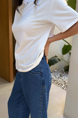 Blue denim barrel jeans featuring silver stud detailing along the pockets and side seams, styled with a white tee.