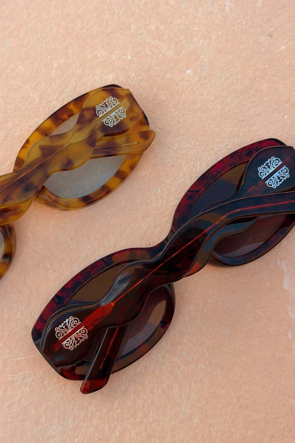 Occhiali da sole Red Wiggle Arm in acetato rosso e tartaruga con astine ondulate su sfondo neutro.