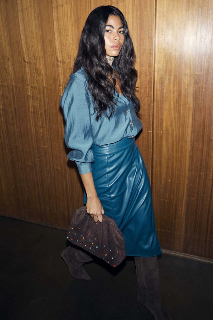 Teal Vegan Leather Jaspre Skirt styled with a matching teal shirt and a brown studded clutch.