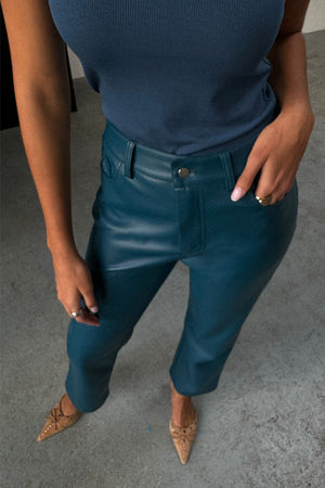 Pantaloni in pelle vegana verde ottanio a gamba dritta con canotta blu a coste e tacchi a punta color cuoio.