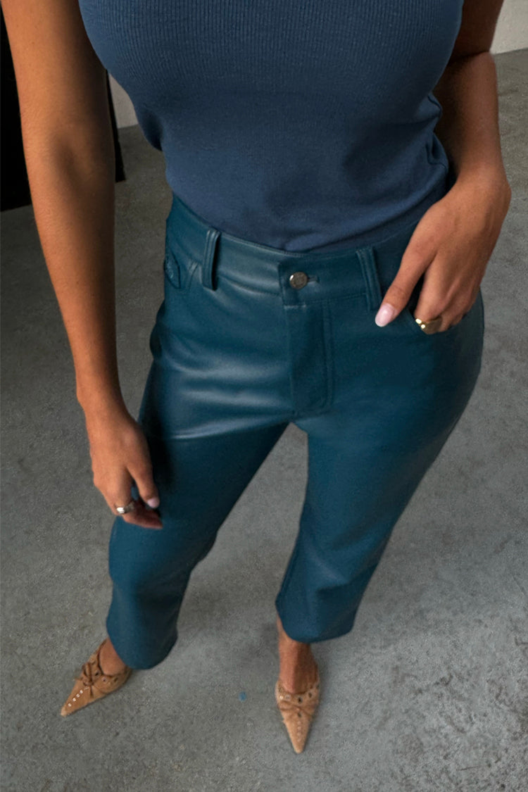 Pantaloni in pelle vegana verde ottanio a gamba dritta con canotta blu a coste e tacchi a punta color cuoio.