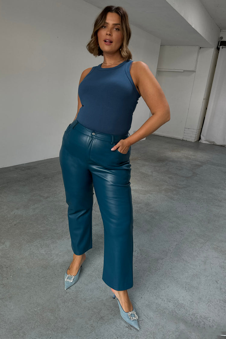Pantaloni in pelle vegana color ottanio a gamba dritta, con top blu e scarpe con tacco gioiello.